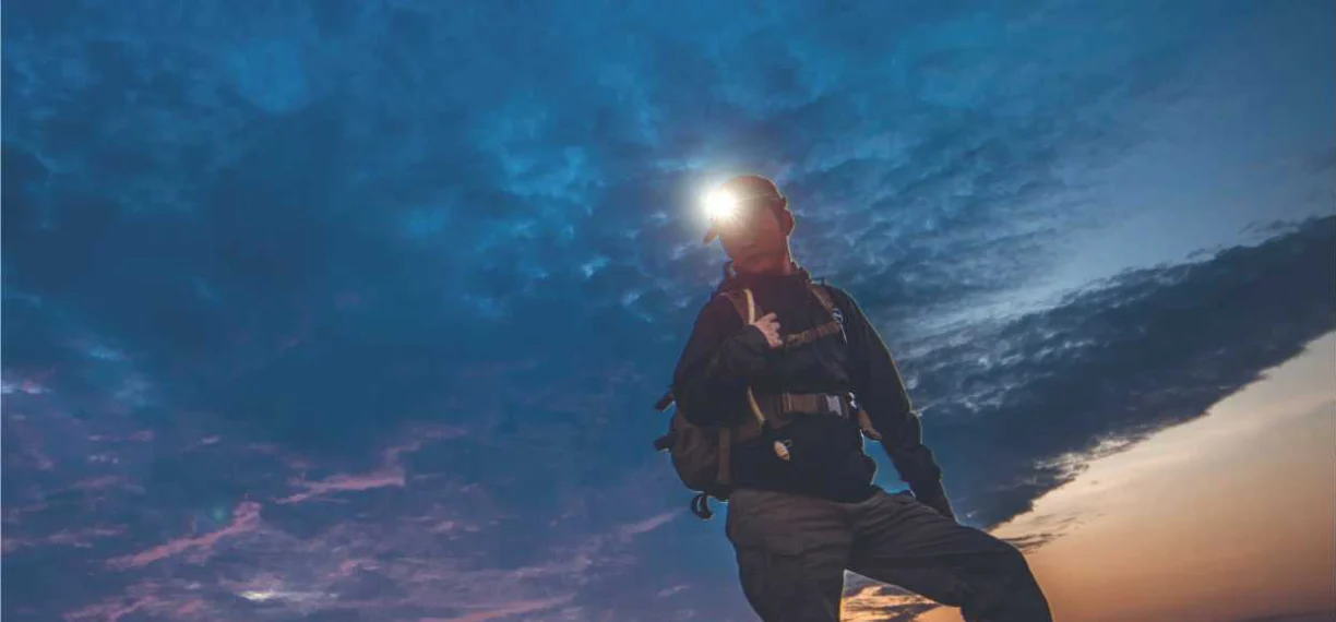 Hiker using a headlamp on a mountain trail at dusk